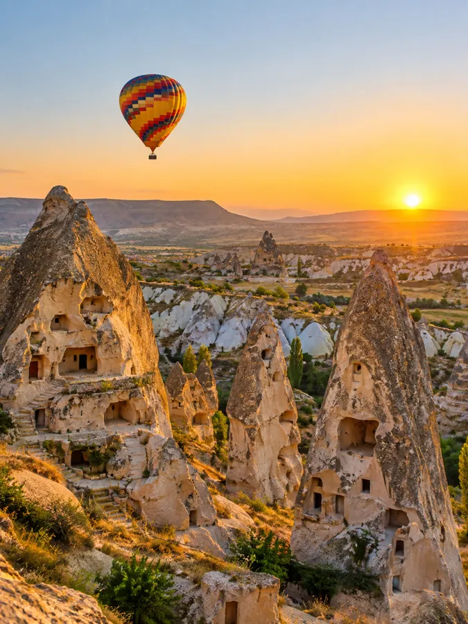 Un globo sobre chimeneas de hadas y casas cueva en Capadocia al amanecer